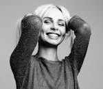 Black and white portrait of a woman smiling joyfully with hands in hair in a studio setting.