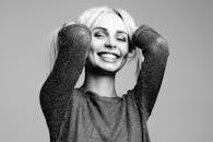 Black and white portrait of a woman smiling joyfully with hands in hair in a studio setting.